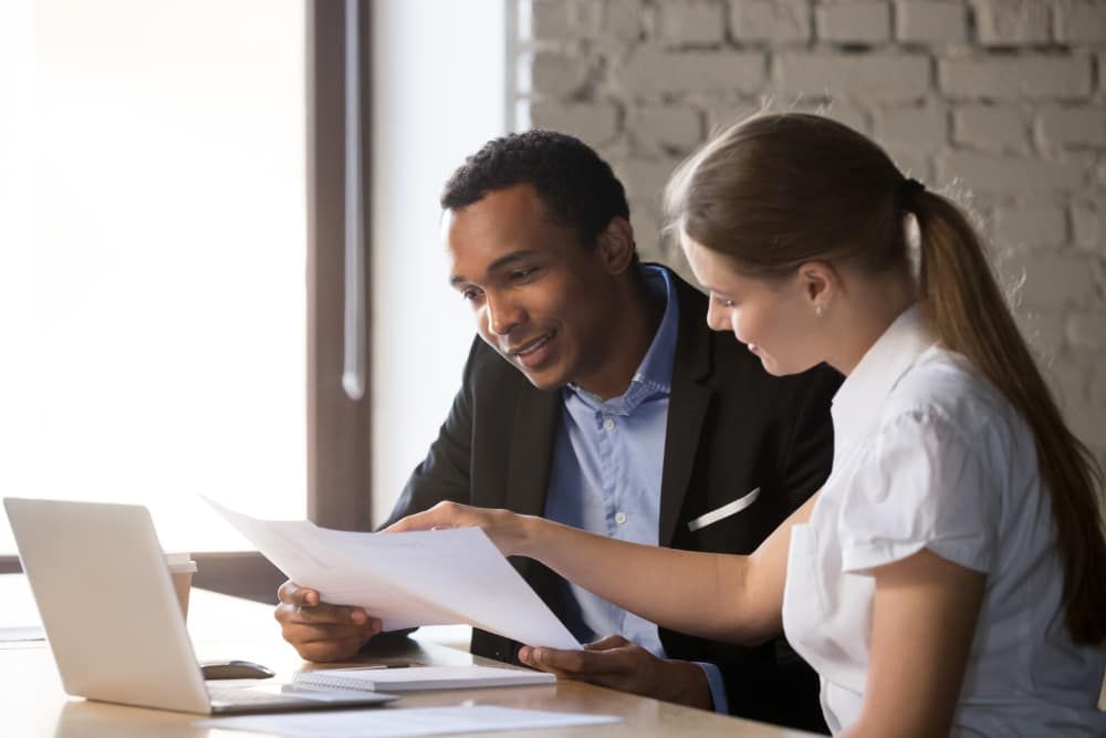 Two people looking at documents and computer